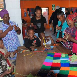Children learning to knit blocks to make a blanket